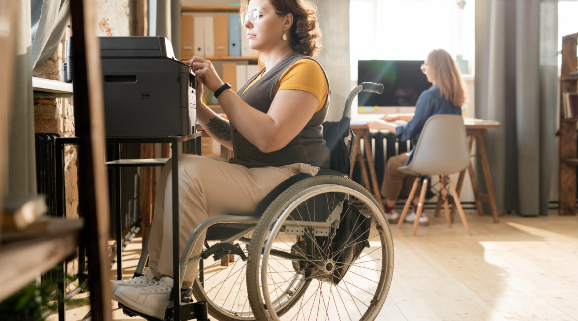 Young Serious Disable Businesswoman Wheelchair Sitting By Xerox Machine Pressing Start Button While Making Copies Documents
